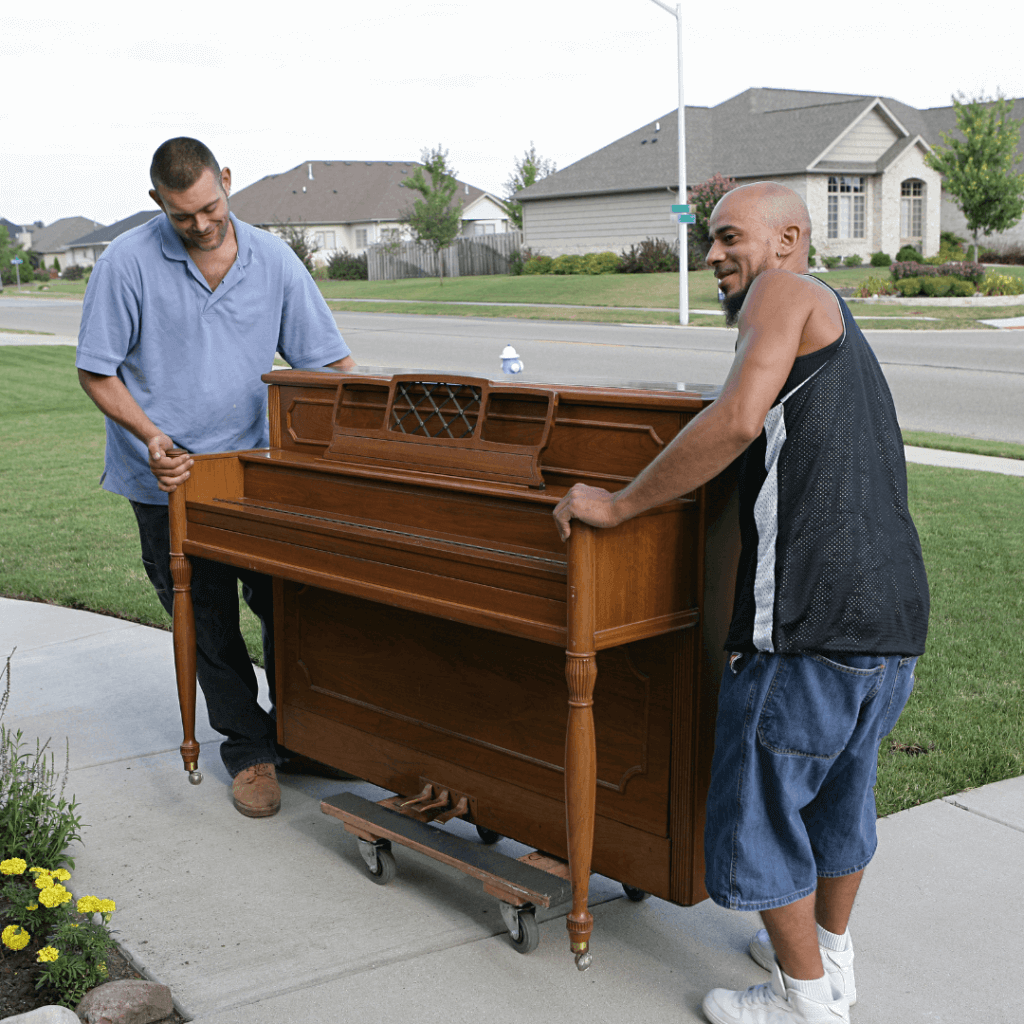 Two men rolling a brown upright piano on a piano dolly.