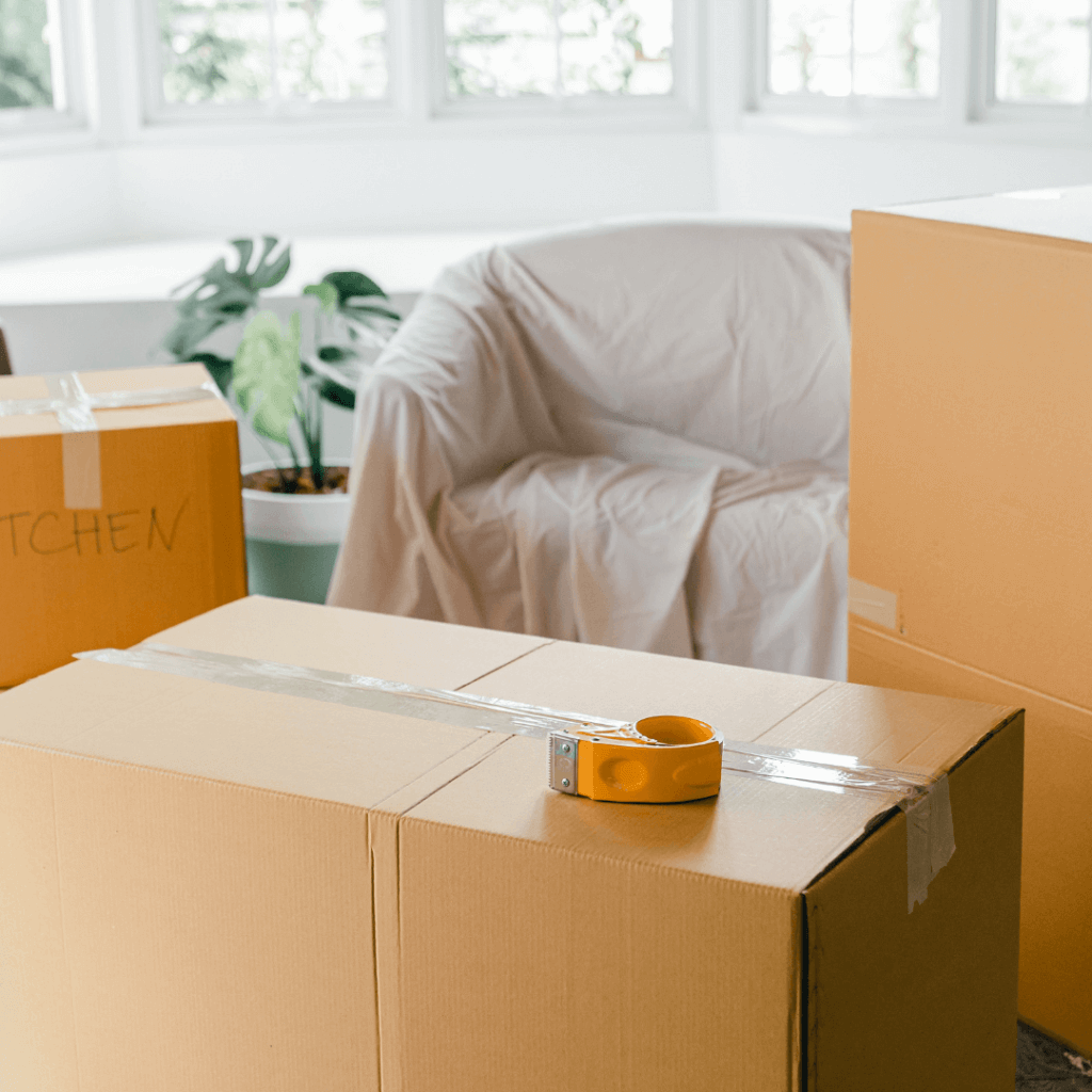 A picture of moving boxes and a chair covered in a white sheet.