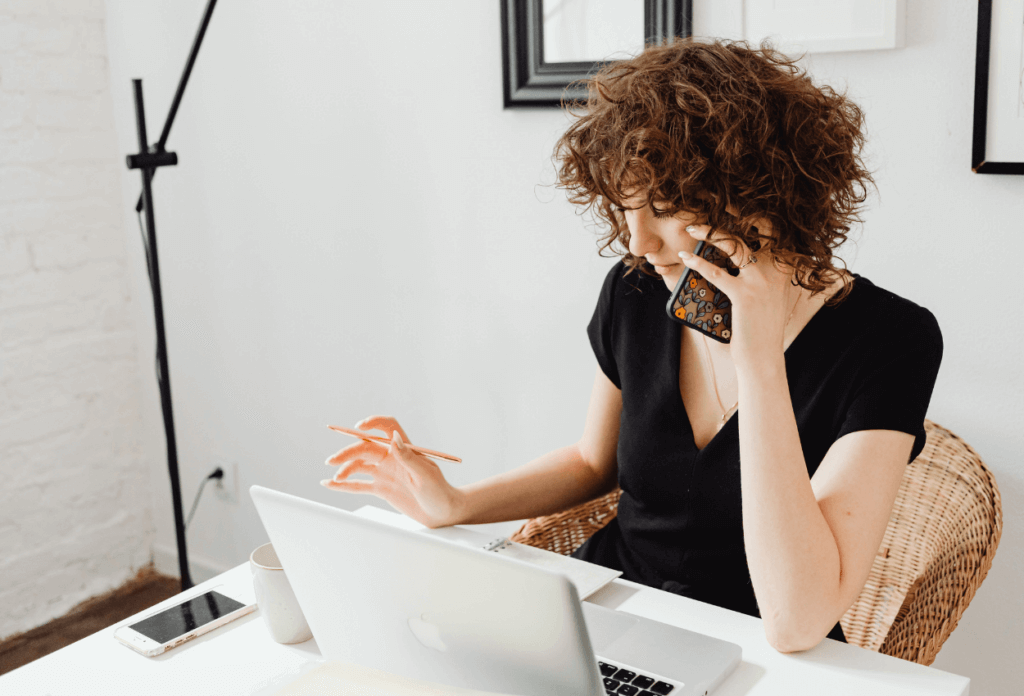 A picture of a woman on the phone sitting at her computer.