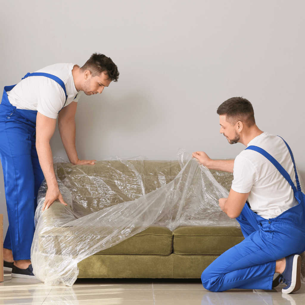 A picture of two movers in Colorado Springs unwrapping a green couch.